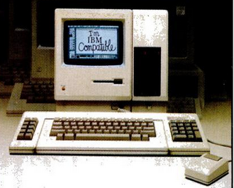 &ldquo;I&rsquo;m IBM Compatible&rdquo; displayed on an original Apple Macintosh with the Mac Charlie addition, including a rectangular PC box attached to the side of the Macintosh, and keyboard extensions including a function keypad on the left side and a numeric keypad on the right side.