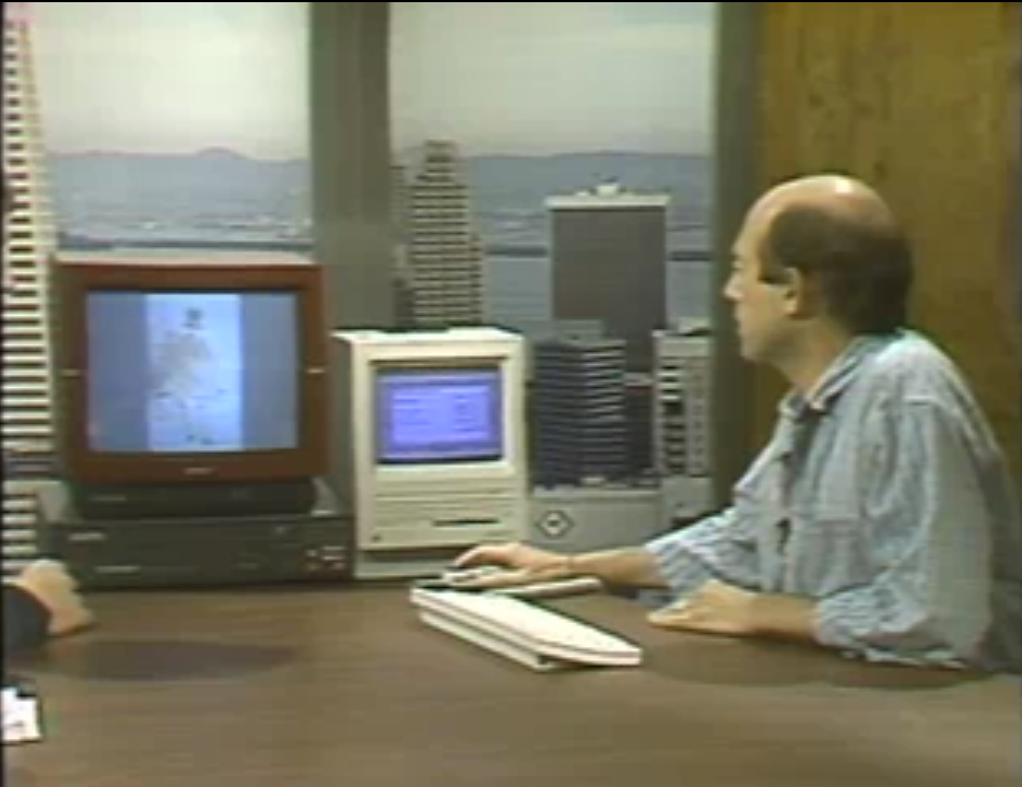 Robert Stein appearing on “Computer Chronicles.” He is seated at the studio desk using a Mouse to control “HyperCard” running on a Macintosh computer. To the left of the Macintosh is a video monitor sitting on top of a Laserdisc player. The video monitor is displaying a piece of art by French painter Clause Monet.